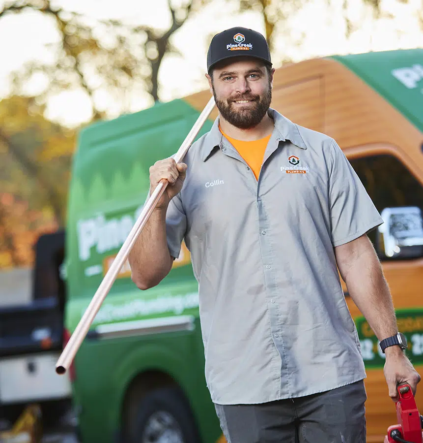 Friendly Pine Creek Plumber holding pipe with truck in background
