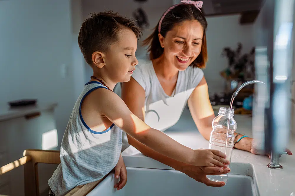 mother and son filling water bottle with clean filtered water from sink